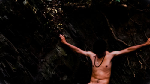 Rear view of shirtless woman standing in cave