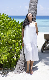 Portrait of young woman standing on rock by sea against sky