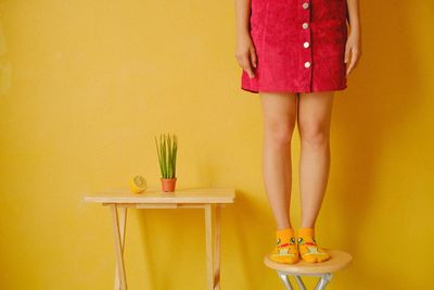 Low section of woman standing on table on yellow background