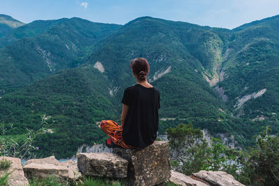 Rear view of man sitting on rock looking at mountains