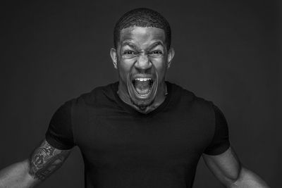 Portrait of angry young man shouting against black background