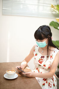 Woman wearing mask using mobile phone at table