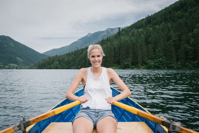 Portrait of smiling woman sitting on lake against sky