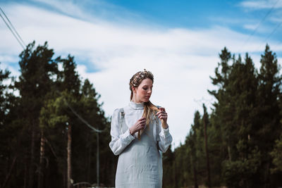 Young woman looking away while standing against trees