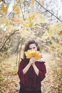 Beautiful girl with curly dark hair in a maroon silk top in an autumn park, smiling at the camera