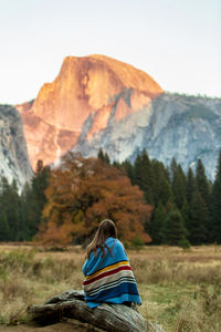 Rear view of woman sitting on field against mountain