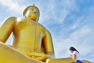 Low angle view of woman praying by buddha statue against sky