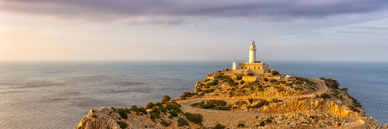 Lighthouse on rock by sea against sky