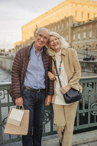 Portrait of happy senior couple leaning on railing in city