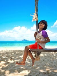 Side view of girl swinging at beach against sky