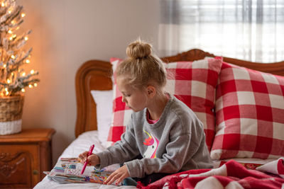 Cute girl drawing on paper while sitting on bed