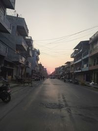 Road amidst buildings against sky during sunset