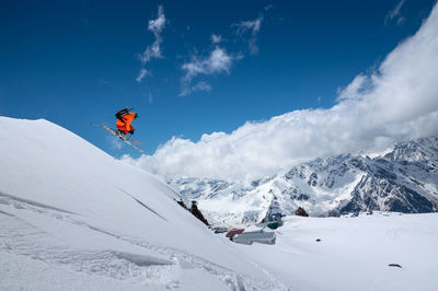 Athlete skier freestyle jumping in orange ski suit in snowy mountains on a sunny day