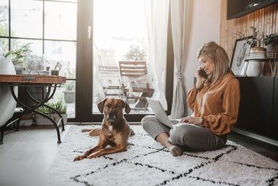 Businesswoman talking on phone while using laptop at home