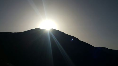 Low angle view of sunlight streaming through silhouette mountain