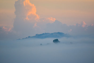 Scenic view of fog covered mountain against sky during sunset