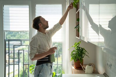 Man in sick leave taking care houseplants at home on kitchen wearing back support belt corset.