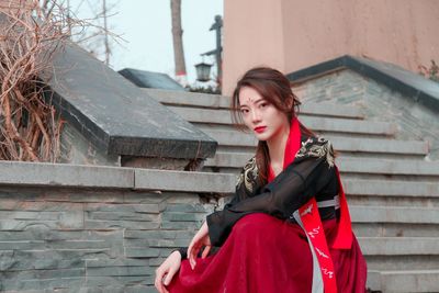 Young woman looking down while sitting against brick wall