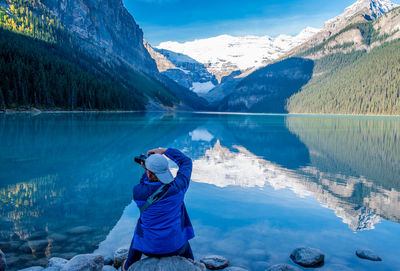 Rear view of man photographing lake against mountains