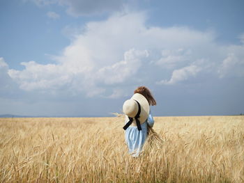 Rear view of children standing on field against sky