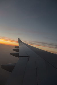 Airplane wing against sky during sunset