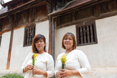 Portrait of smiling woman holding glass while standing against building