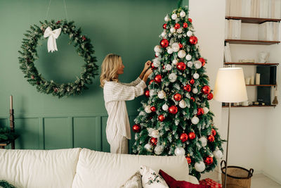 Elegant young woman decorates a christmas tree in a bedroom living room interior.