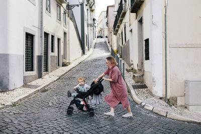 Mother walking with male toddler in baby stroller on street