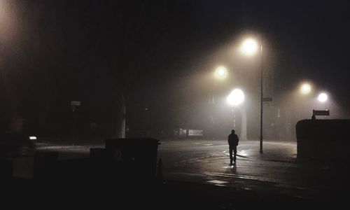 Silhouette man with illuminated street light against sky at night