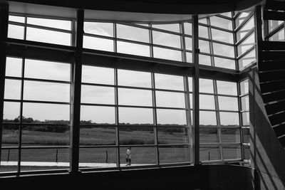 Person walking on field against sky seen through window