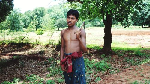 Portrait of shirtless young man standing on field