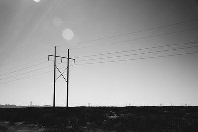 Electricity pylons on field against clear sky