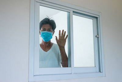 Portrait of mature man wearing flu mask seen through window