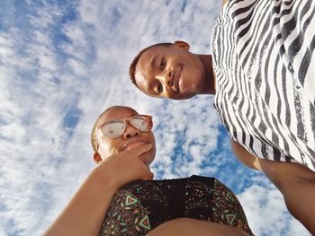 Directly below shot of friends standing against cloudy sky