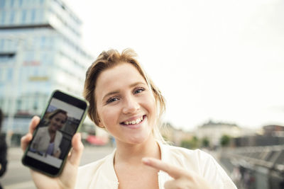 Portrait of happy woman showing photograph in mobile phone