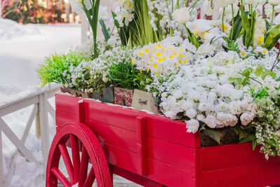 Red wooden wheelbarrow with wooden boxes full of blooming artificial flowers. 