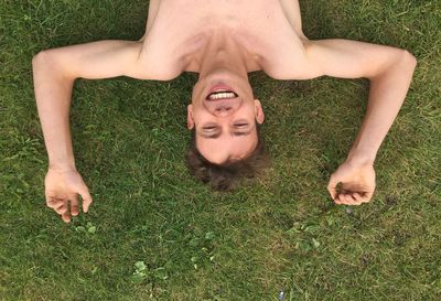 Directly above shot of happy shirtless man lying on grassy field