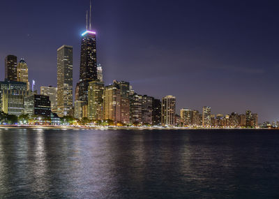 Illuminated modern buildings against clear sky by river