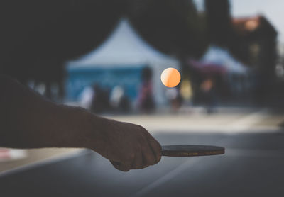 Cropped image of hand holding table tennis racket during sunset