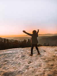 Woman with arms outstretched standing on land during sunset