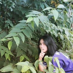 Portrait of woman with finger on lips amidst plant