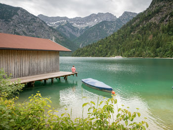 Man sitting on jetty over lake against mountain