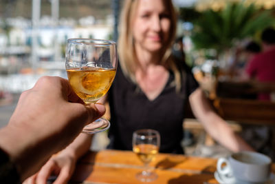 Cropped hand of friend holding whiskey glass against woman at restaurant