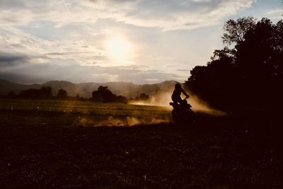 Silhouette person riding on field against sky during sunset