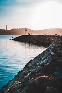 Scenic view of groyne by sea during sunset