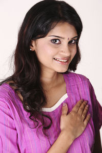 Portrait of smiling young woman with hand on chest against white background