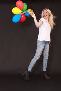 Smiling woman with balloons walking against wall