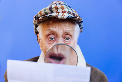 Close-up of senior woman examining paper with magnifying glass against blue background