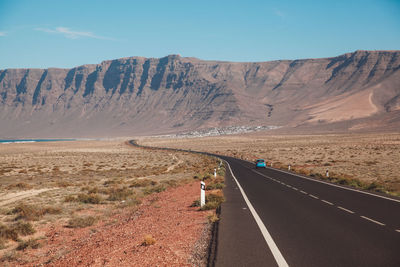 Car on road amidst field leading towards mountains