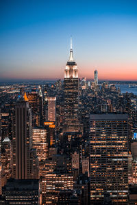 High angle view of illuminated empire state building and cityscape against clear blue sky at night